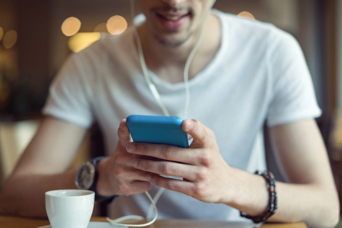 Young man using smartphone with earphones at café