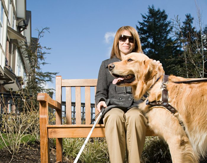 Young woman sat on bench with guide dog and stick